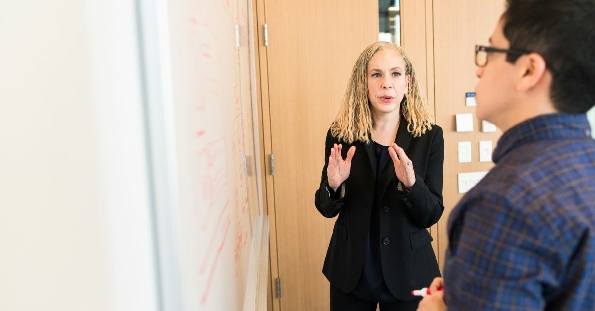 A professional woman presents an idea on the whiteboard to her coworker