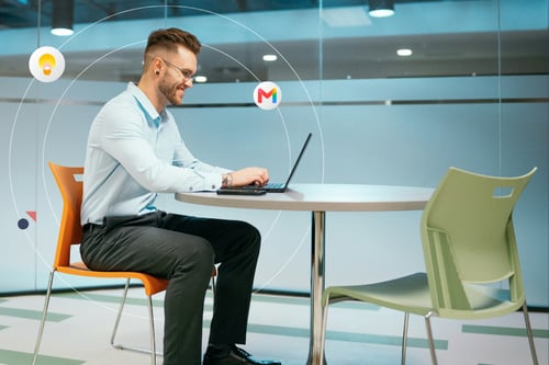 A professional man with glasses sits at a table with his laptop