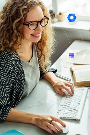 A young woman with curly hair and glasses looks at a computer off screen