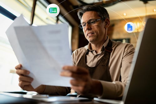 A middle aged man with glasses looks at two pieces of paper