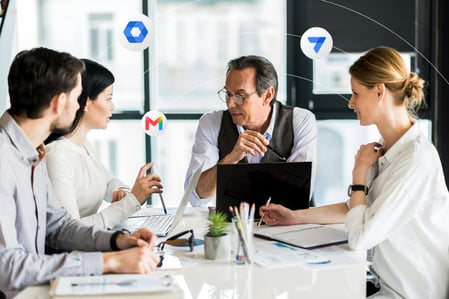 Four people site gathered around a conference table with their laptops and notebooks