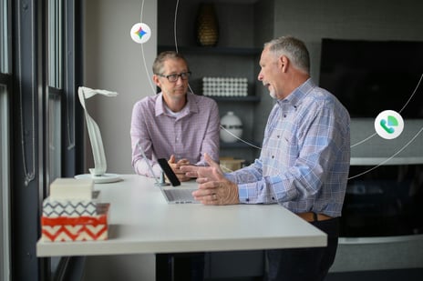 Two men talk over a standing desk and laptop 