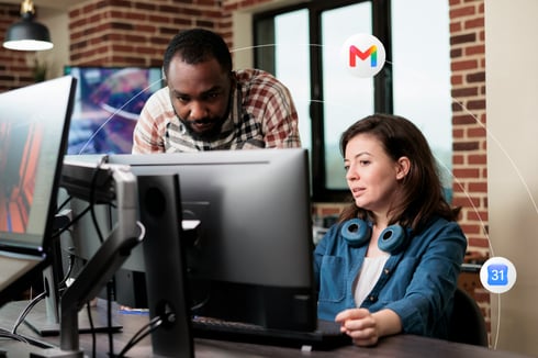 Two office workers looking at the same desktop monitor 