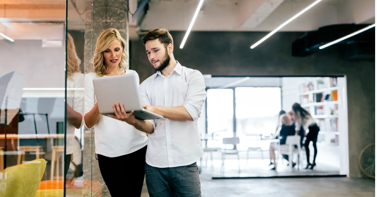 Coworkers looking at a laptop together in a modern office with an open floor plan 