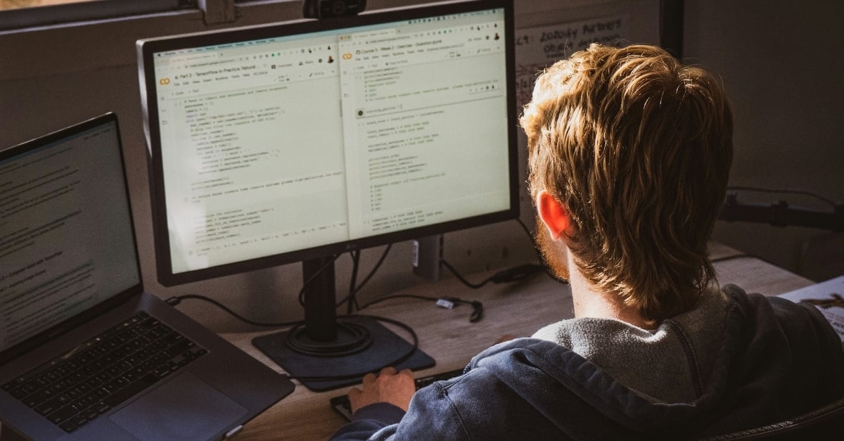 A young professional facing away from the camera reviews code in a modern office setting