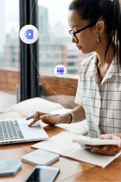 A young woman with glasses looks down at her laptop while doing paperwork